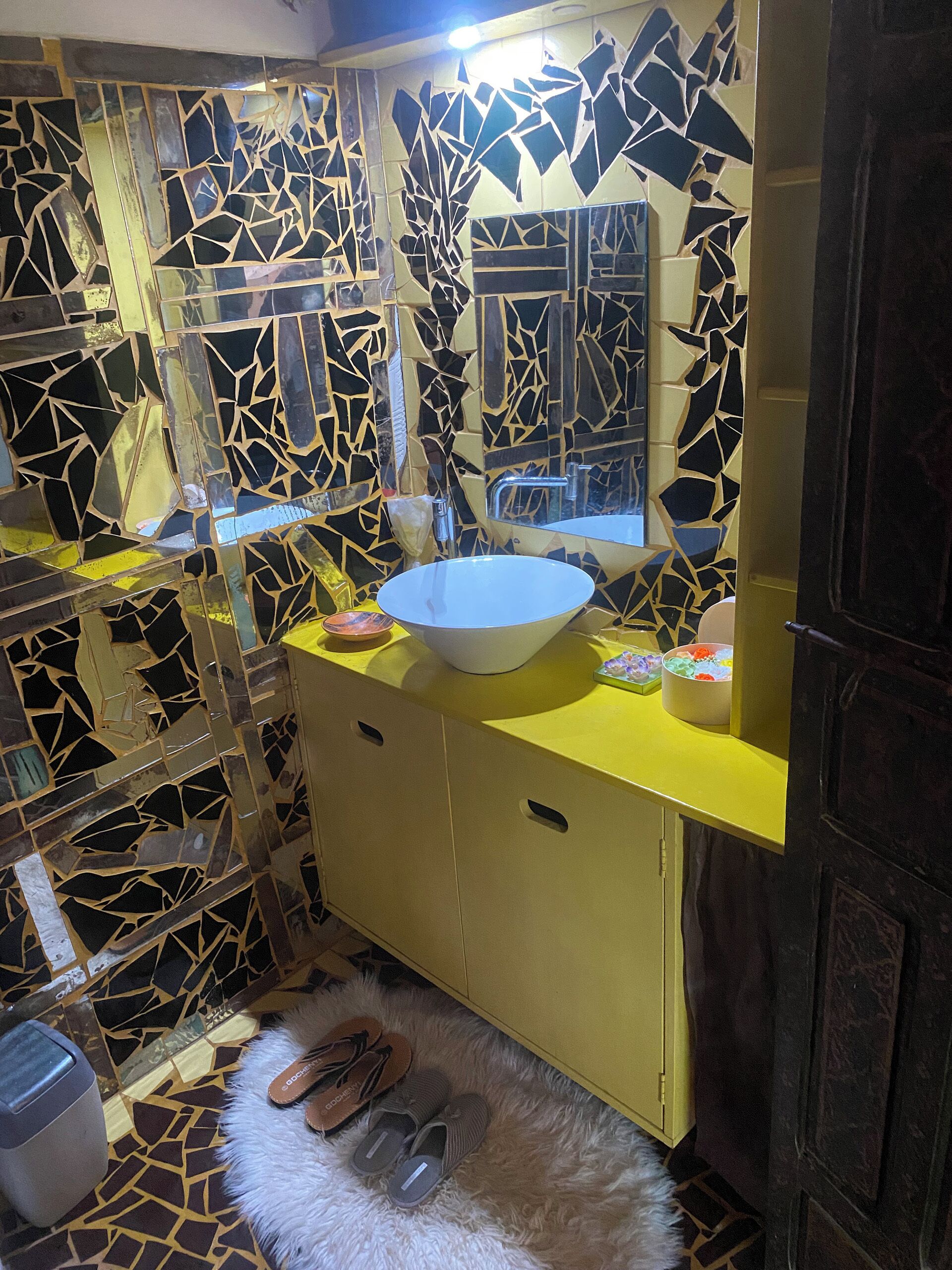 A bathroom with a mosaic tile wall, a white sink, and a yellow vanity.