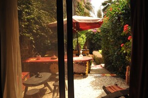 An outdoor patio area with a round table and chairs, a small fountain, and a red umbrella.