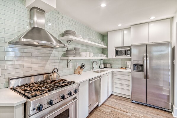 Una cucina moderna con piano cottura, forno a microonde e frigorifero in acciaio inox, mobili bianchi e zoccolo verde chiaro.