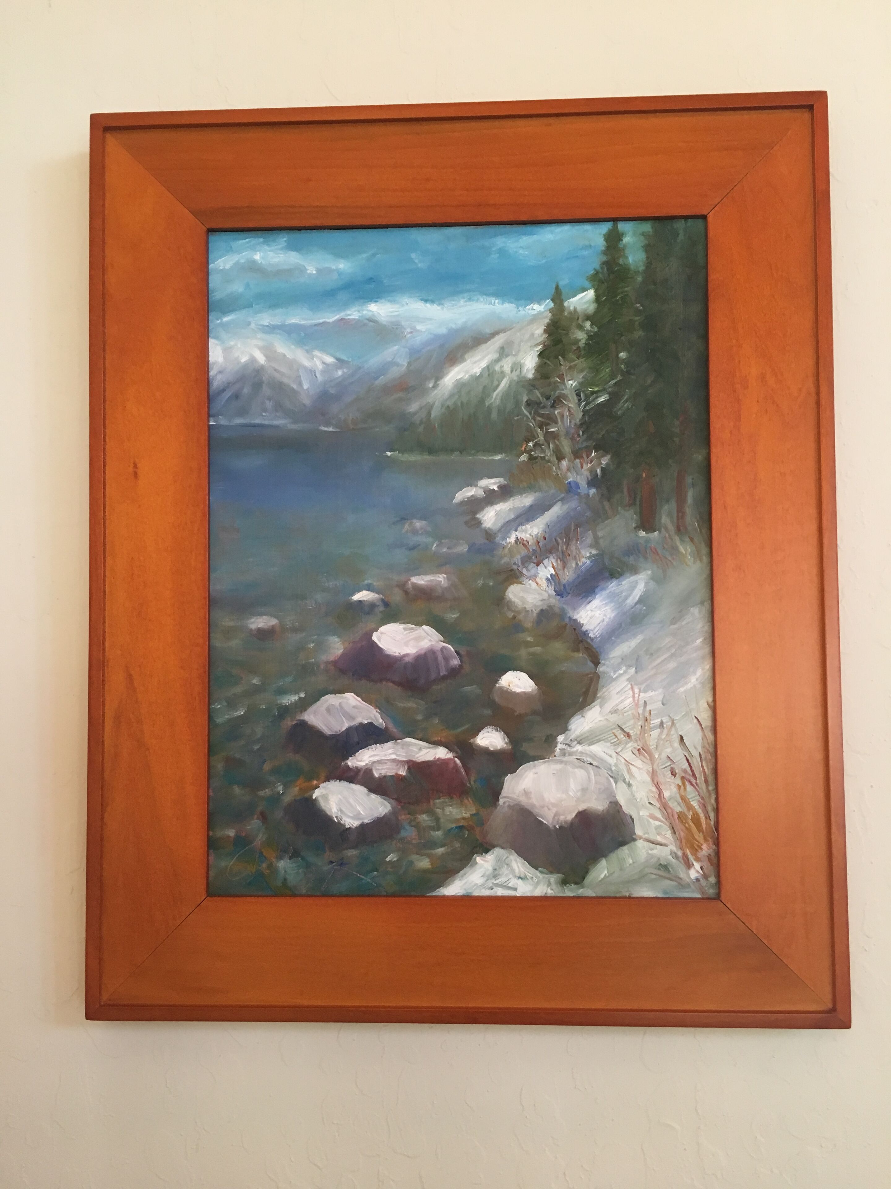 A framed landscape painting of a mountain lake with rocks and trees.