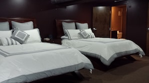 Two beds with white bedding and grey accents, each with a wooden headboard, are positioned in this cozy space.