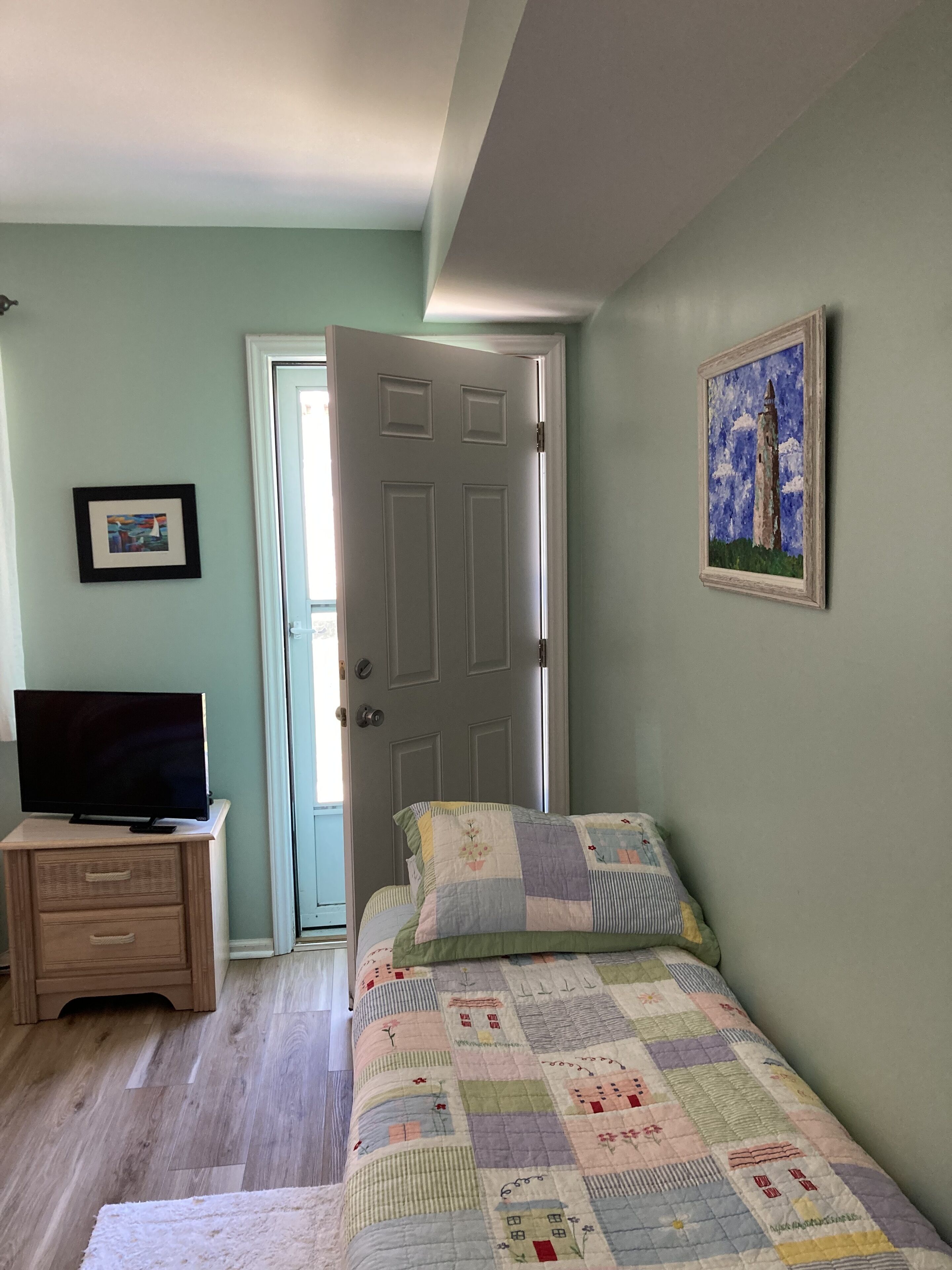 A bedroom with a bed, a dresser, a television, a door, and a painting on the wall.