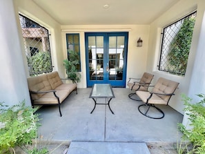 A covered patio area with a blue door, beige sofas, and a central table.