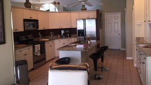 A kitchen with white cabinets, a microwave, a refrigerator, a coffee maker, and a ceiling fan. - Villa Alegria, Your Home Away From Home! (Cape Coral)