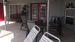 A covered patio area with a dining table, chairs, a ceiling fan, and a red door. - Villa Alegria, Your Home Away From Home! (Cape Coral)