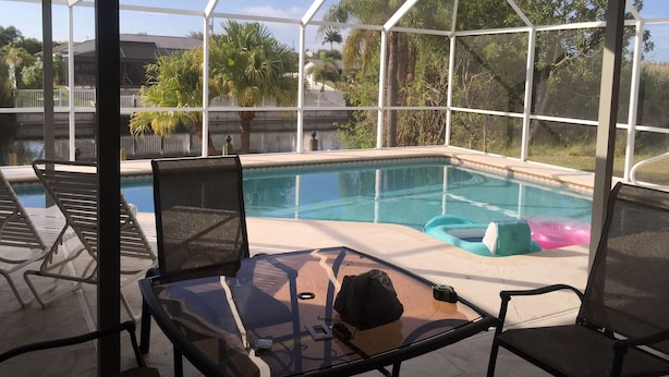 A covered outdoor pool area with lounge chairs and a glass table. - Villa Alegria, Your Home Away From Home! (Cape Coral)