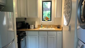 Une cuisine de taille réduite avec des meubles blancs, un carrelage noir et blanc, une fenêtre donnant sur un espace verdoyant et un lave-linge.