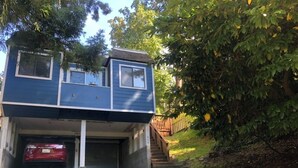 Une maison bleue de plain-pied avec un garage, une voiture rouge garée à l’intérieur et un escalier menant à l’étage supérieur.