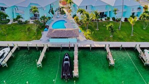 Een resort met meerdere blauwe gebouwen, een centraal zwembad en een steiger met boten.