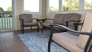 Een overdekt terras met twee beige stoelen en een kleine tafel, een kamerbreed tapijt en uitzicht op een speeltuin door de balustrade.