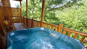 Un jacuzzi en una terraza de madera con vistas a árboles.