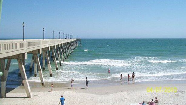 A pier extending into the ocean with people walking along it. - Beautiful 2nd floor unit with ocean views and 2 minute walk to the beach. (Wrightsville Beach)