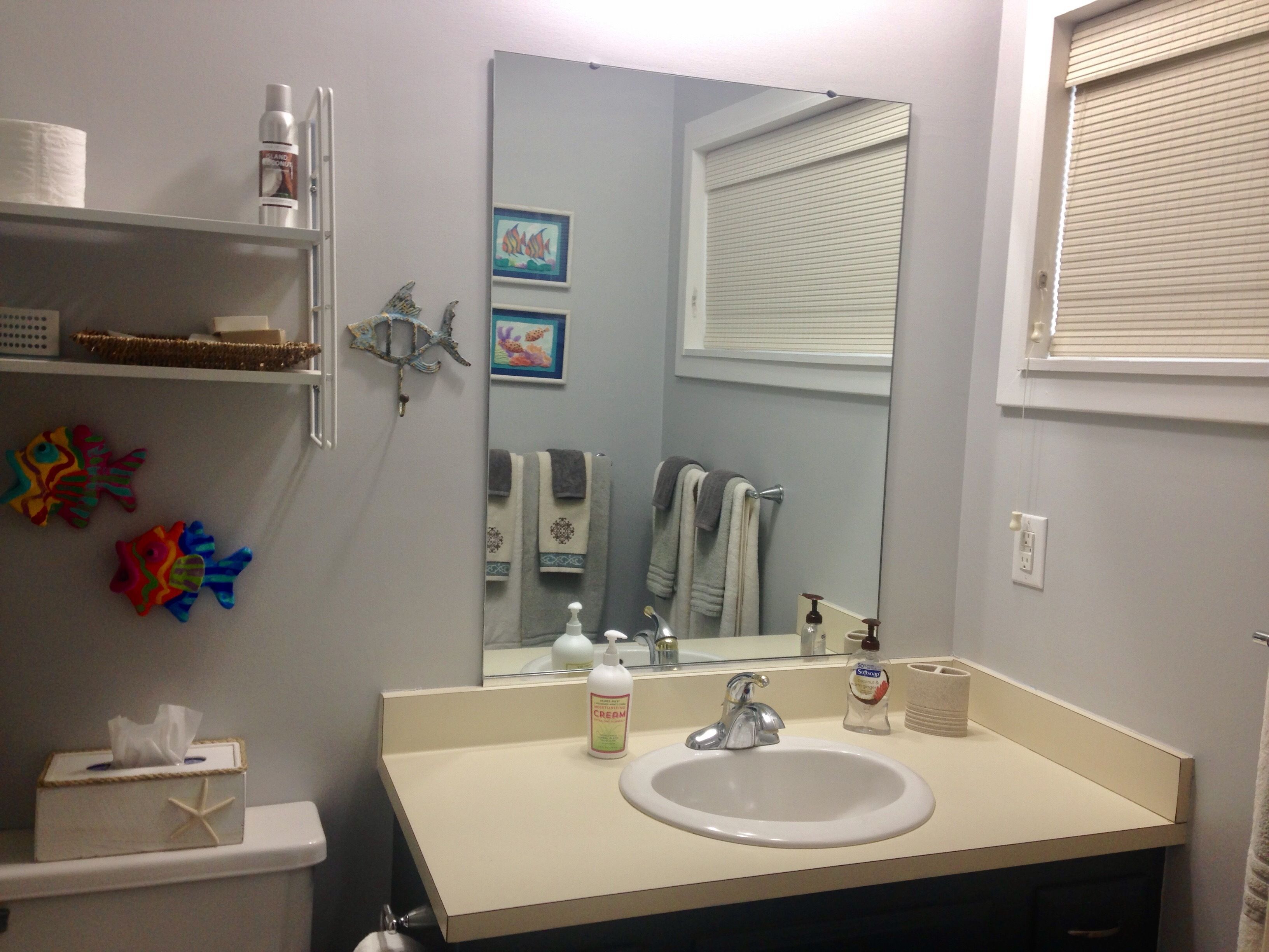 A bathroom with a sink, mirror, shelves with toiletries, and decorative fish figures.