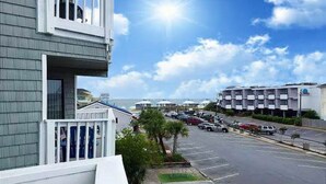 A parking lot with several cars, a building with a balcony, and a clear sky. - Beautiful 2nd floor unit with ocean views and 2 minute walk to the beach. (Wrightsville Beach)