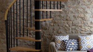 A spiral staircase with wooden steps and black railings, a stone wall, and a sofa with patterned cushions. - Charming Cottage Set In The Loire Valley Just Minutes From Sancerre (Feux)