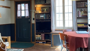 A cozy room with a wooden ceiling, a dining table with a red tablecloth, a bookshelf, and a door with checkered curtains. - Cozy one bedroom Hideaway Resort cabin #6 (Chippewa Falls)