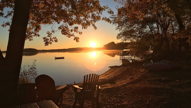 A lakeside view with a wooden bench and a boat docked on the shore. - Cozy one bedroom Hideaway Resort cabin #6 (Chippewa Falls)