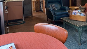 A cozy room with a wooden ceiling, a dining table with a red tablecloth, a black leather chair, and a small wooden table with a lamp. - Cozy one bedroom Hideaway Resort cabin #6 (Chippewa Falls)