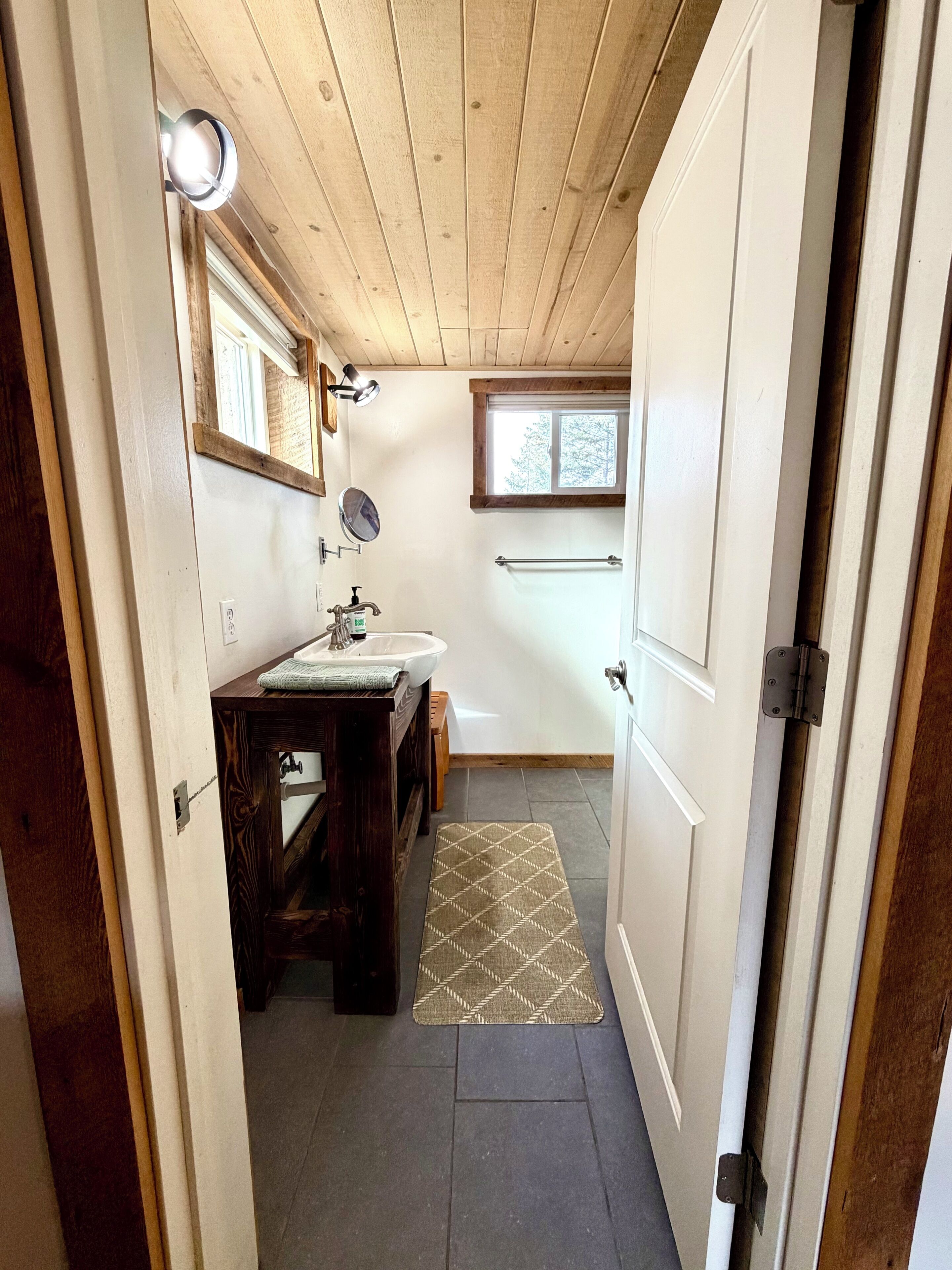 A bathroom with a wooden ceiling, a window, a sink, a mirror, and a towel rack.