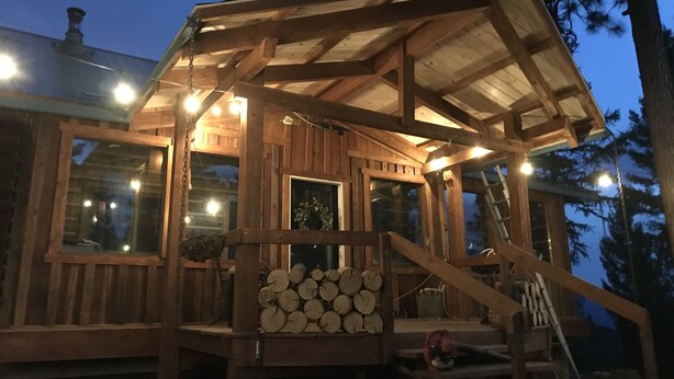 Una cabaña de madera con porche cubierto, ventanas amplias y una pila de leña.