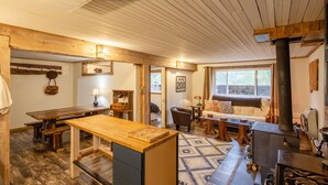 Un interior rústico con una mesa de comedor de madera, una zona de estar acogedora y una estufa de leña.