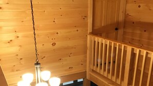 Interior de una cabaña de madera con candelabro, paredes de madera y un balcón.