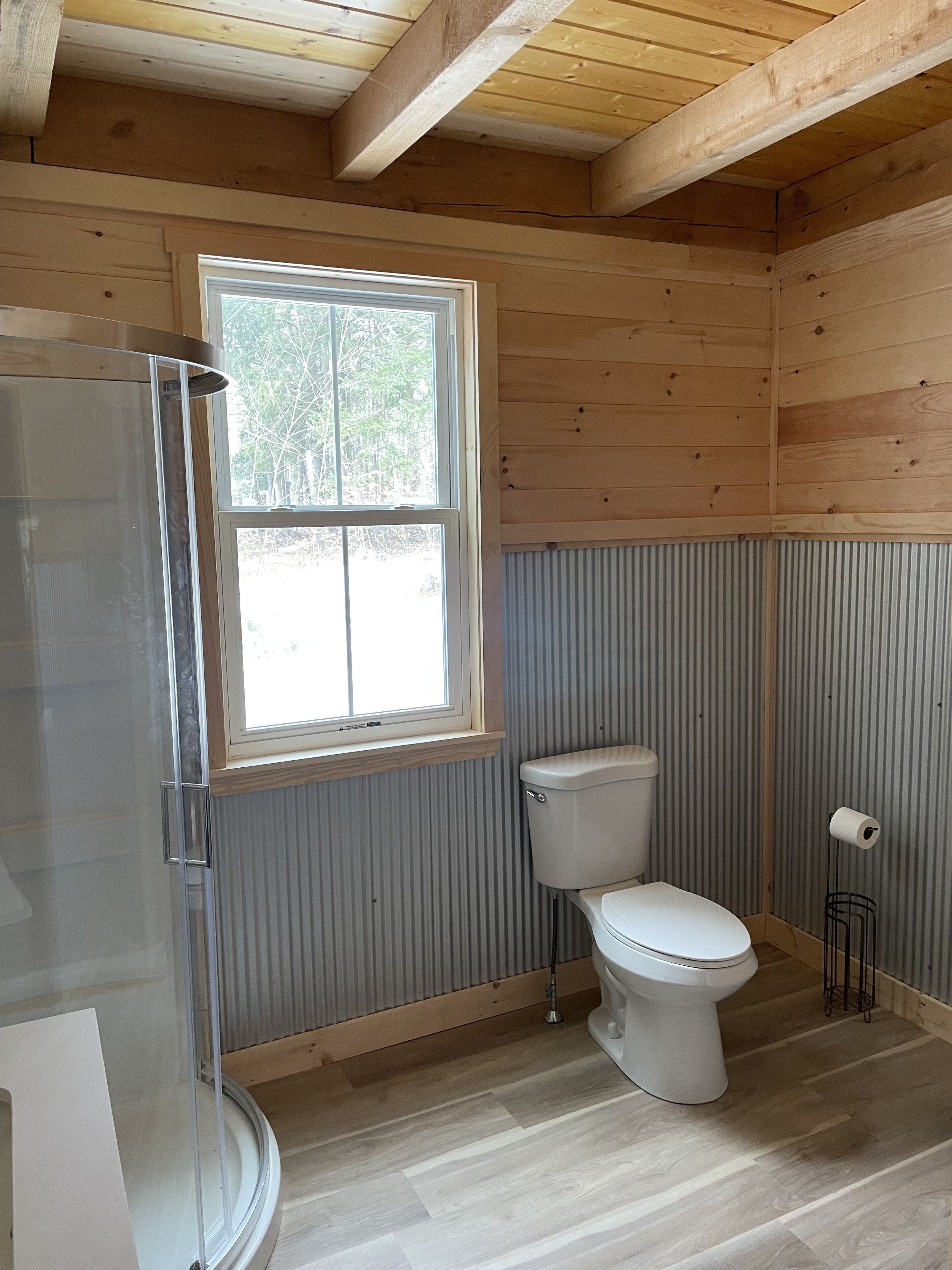 Une salle de bain avec un plafond en bois, une fenêtre, des toilettes et un espace douche.
