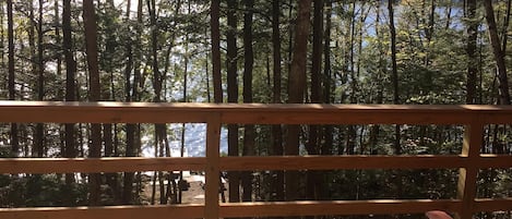 A wooden deck with a railing overlooking a forested area and a body of water.