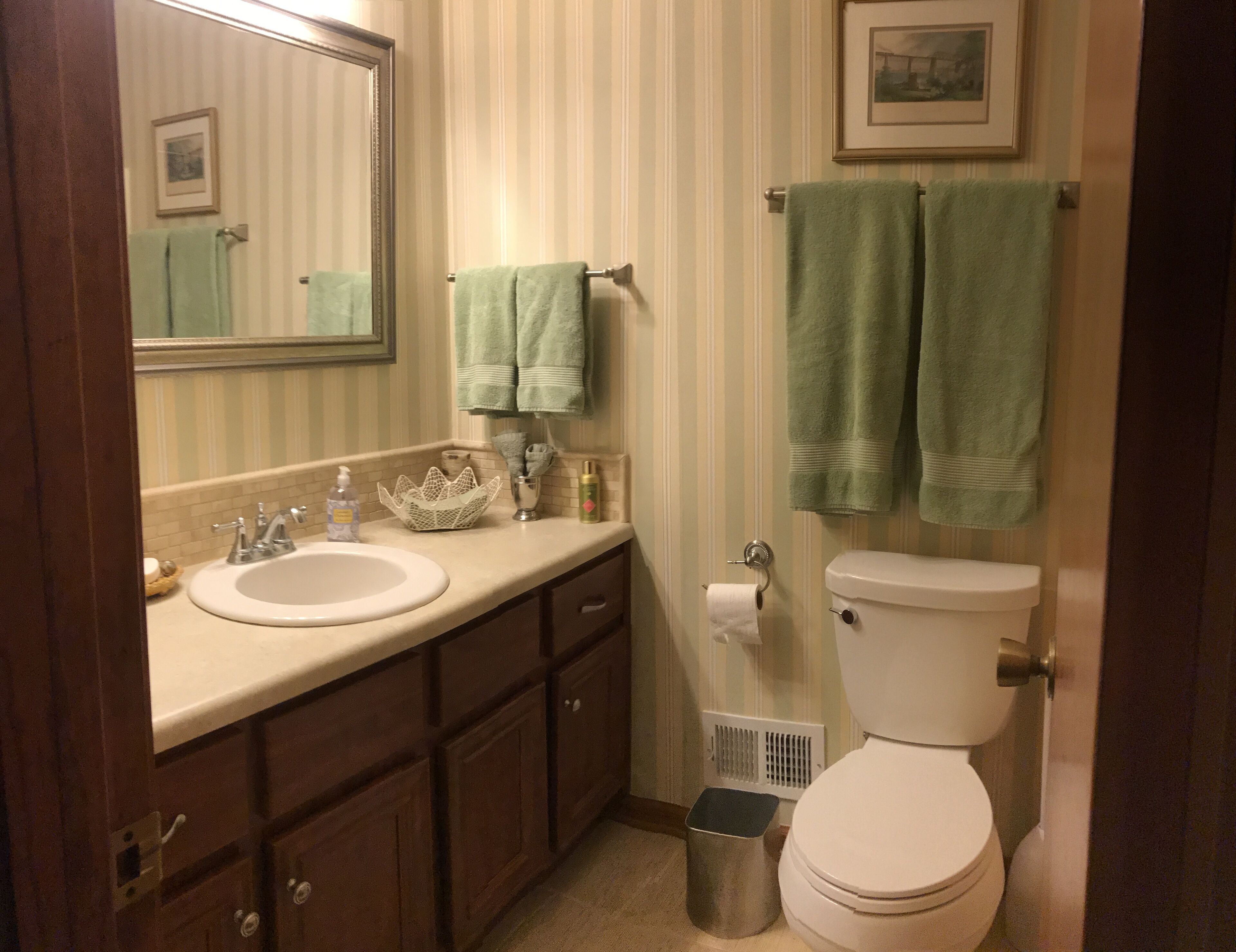 A bathroom with a sink, mirror, toilet, and towels.