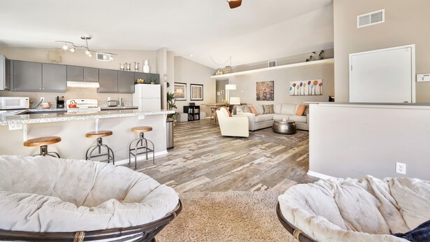 A modern kitchen with bar stools, a dining area with a sofa, and a ceiling fan. - Fabulous Location @ Rancho Relaxo  (La Quinta)