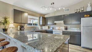 A modern kitchen with granite countertops, stainless steel appliances, and a bar area with stools. - Fabulous Location @ Rancho Relaxo  (La Quinta)