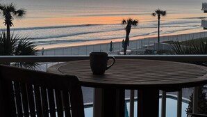 Un balcón con mesa y sillas con vistas a una playa al atardecer.