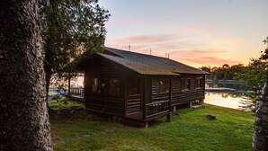 A log cabin with a porch, situated by a lake, surrounded by trees.