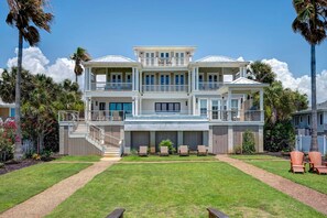 A two-story beachfront house with a balcony, a covered porch, and a well-maintained lawn.
