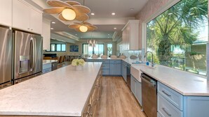 A modern kitchen with a large island, stainless steel appliances, and a view of palm trees.