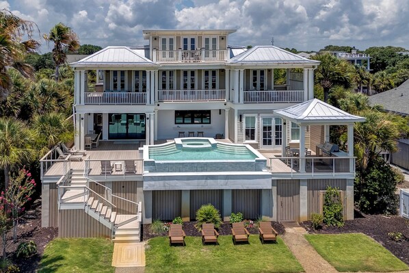 A two-story house with a large swimming pool, multiple decks, and a covered outdoor seating area.