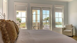A bedroom with a large bed, a chair, and a view of the ocean through large windows.