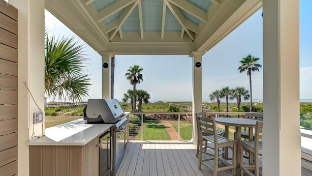 A covered outdoor area with a grill, seating, and a view of the beach.