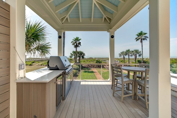 A covered outdoor area with a grill, seating, and a view of the beach.
