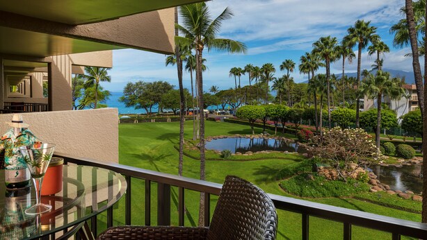 A balcony with a view of a golf course, palm trees, and a body of water. - OCEAN VIEW - SLEEP 6! -Single Level - Family Room -No Stairs-Steps to Beach! (Kihei)