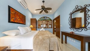 Une chambre à coucher comprenant un lit, un ventilateur de plafond, un miroir fixé au mur et une fenêtre décorative.