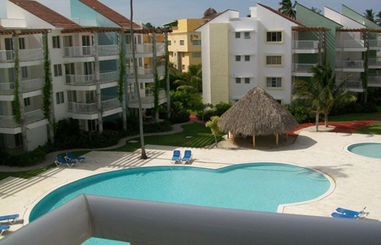A resort with a large swimming pool, lounge chairs, and a thatched-roof structure.