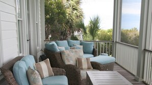 A covered porch with wicker furniture and a wooden table. - Beautiful Oceanfront 5 Bedroom Home With Pool  (Isle of Palms)