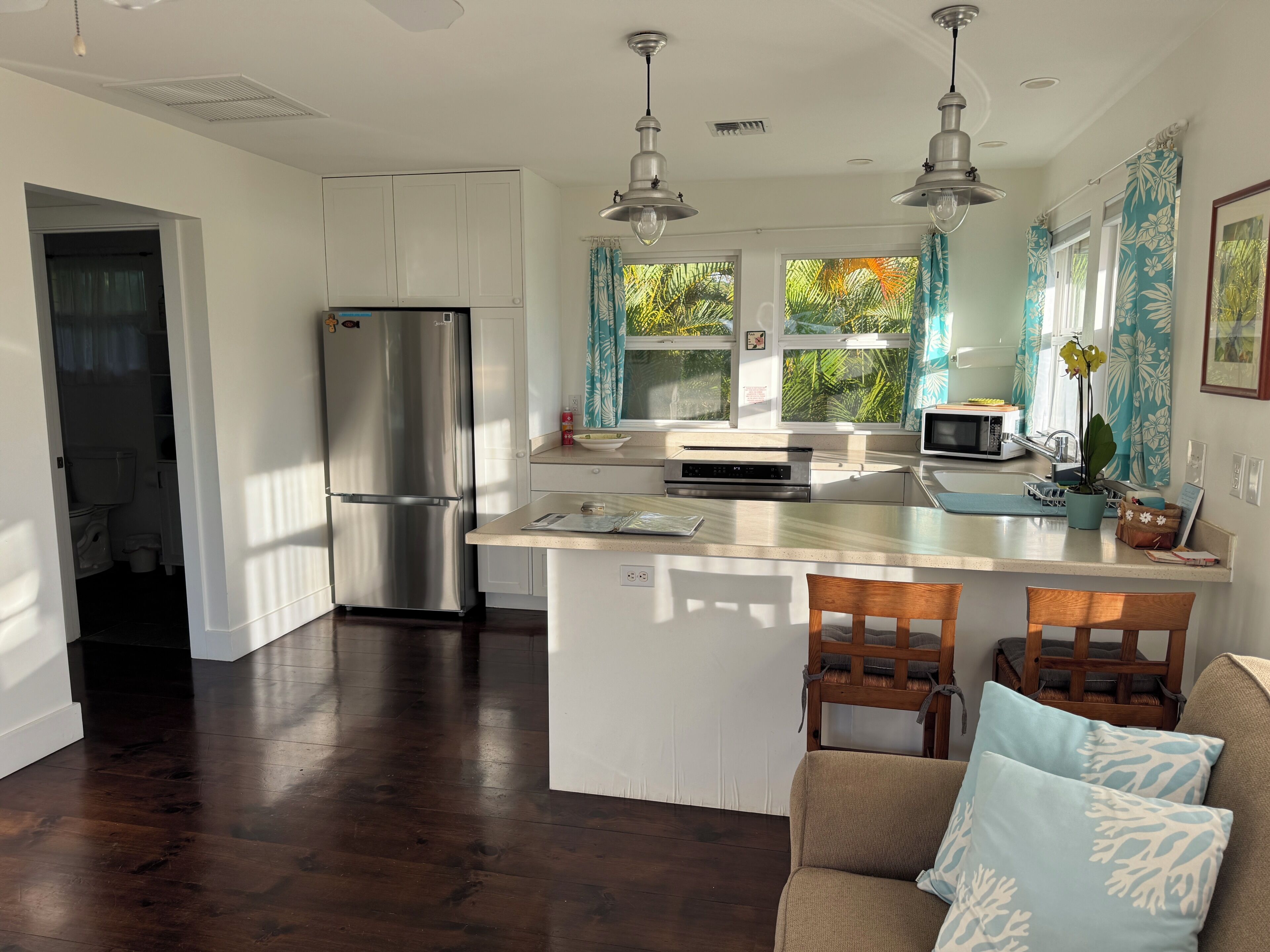A modern kitchen with a central island, stainless steel appliances, and a view of greenery outside.
