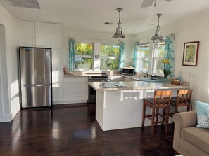 A modern kitchen with a central island, stainless steel appliances, and large windows. - North Shore Ocean-View Garden Cottage near Paia – Maui by the Sea (Paia)