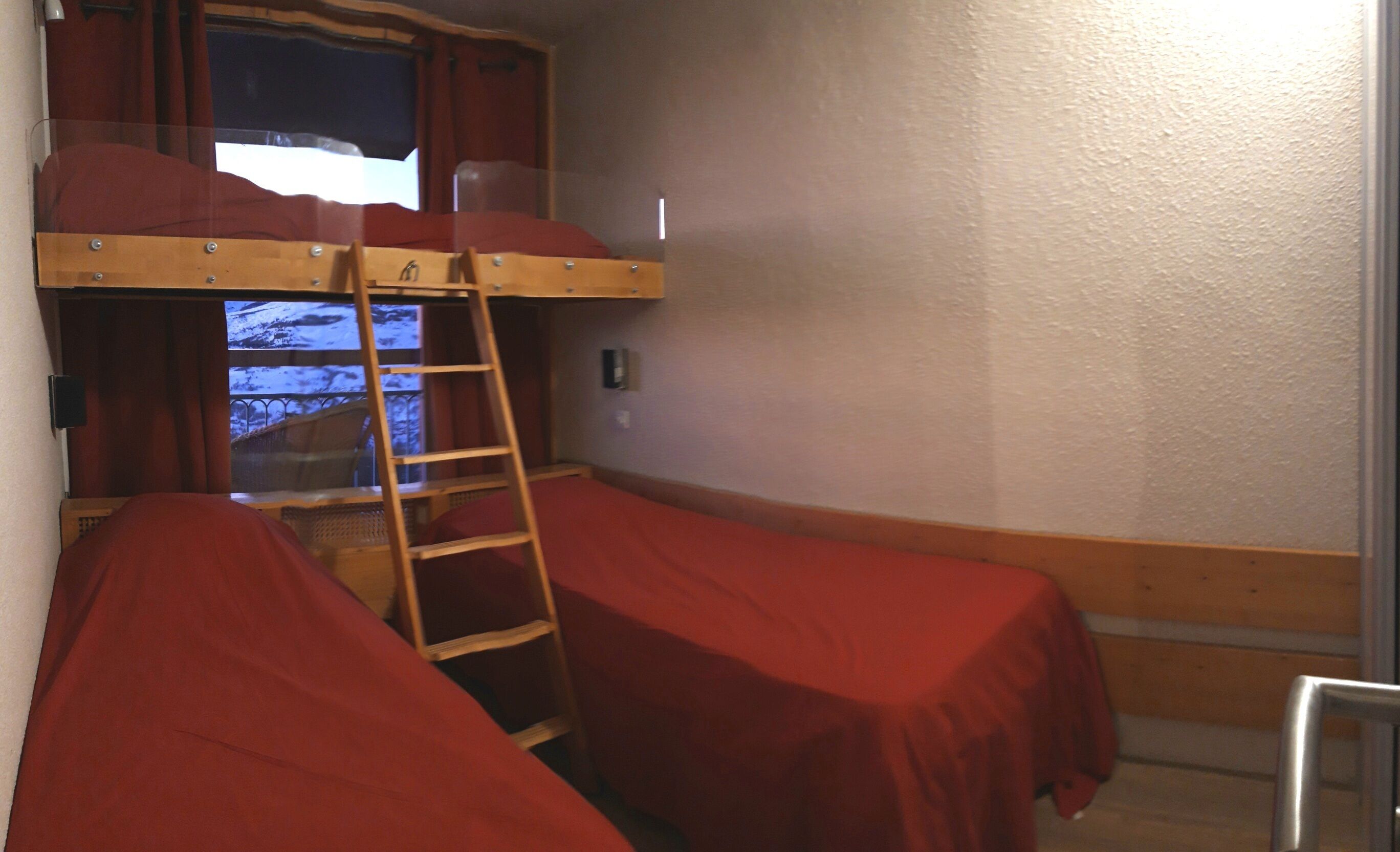 Een slaapkamer met een stapelbed, rode beddengoed en een raam met gordijnen.
