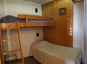 A bunk bed with a ladder, a single bed, wooden walls, a small picture, and a power outlet.