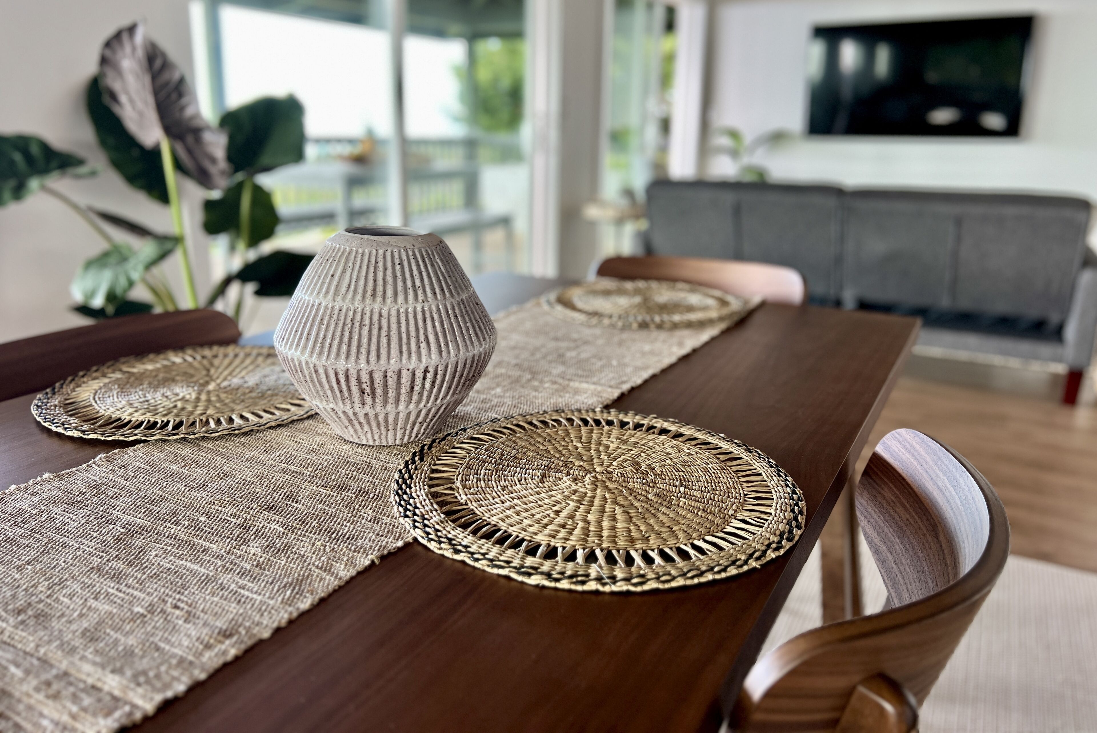 Une table à manger avec des sets de table en fibres tressées et un vase.