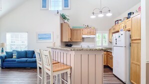 Eine Küche mit Holzausstattung, einer zentralen Kochinsel mit Barhocker, einem Kühlschrank und einem Essbereich mit blauem Sofa und Stühlen.