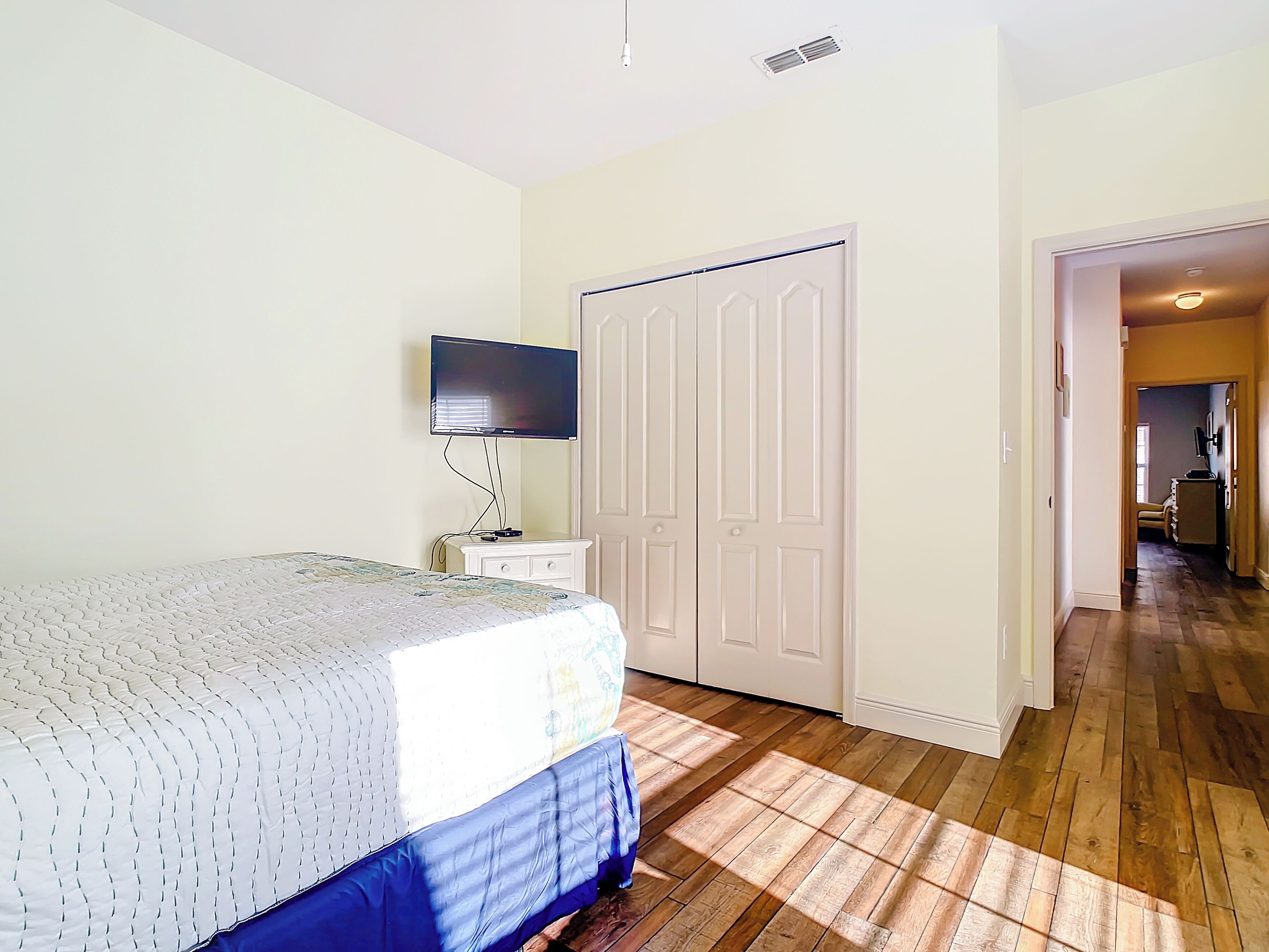 A bedroom with a bed, a television, a wardrobe, and a hallway leading to another room.